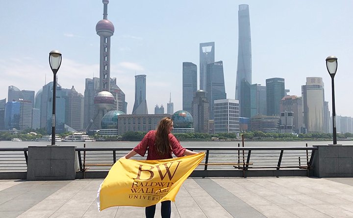Business major Gwyn Dubel in China holding a Baldwin Wallace flag in front of a skyline.